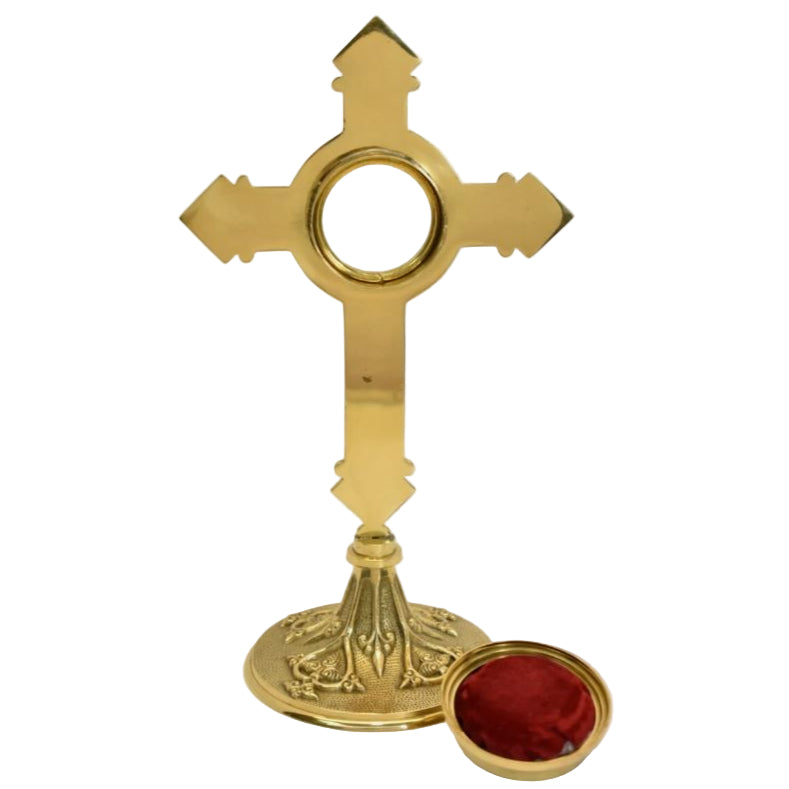 A polished brass cross-shaped reliquary with a round relic compartment and an ornate base. Back view showing the door removed.