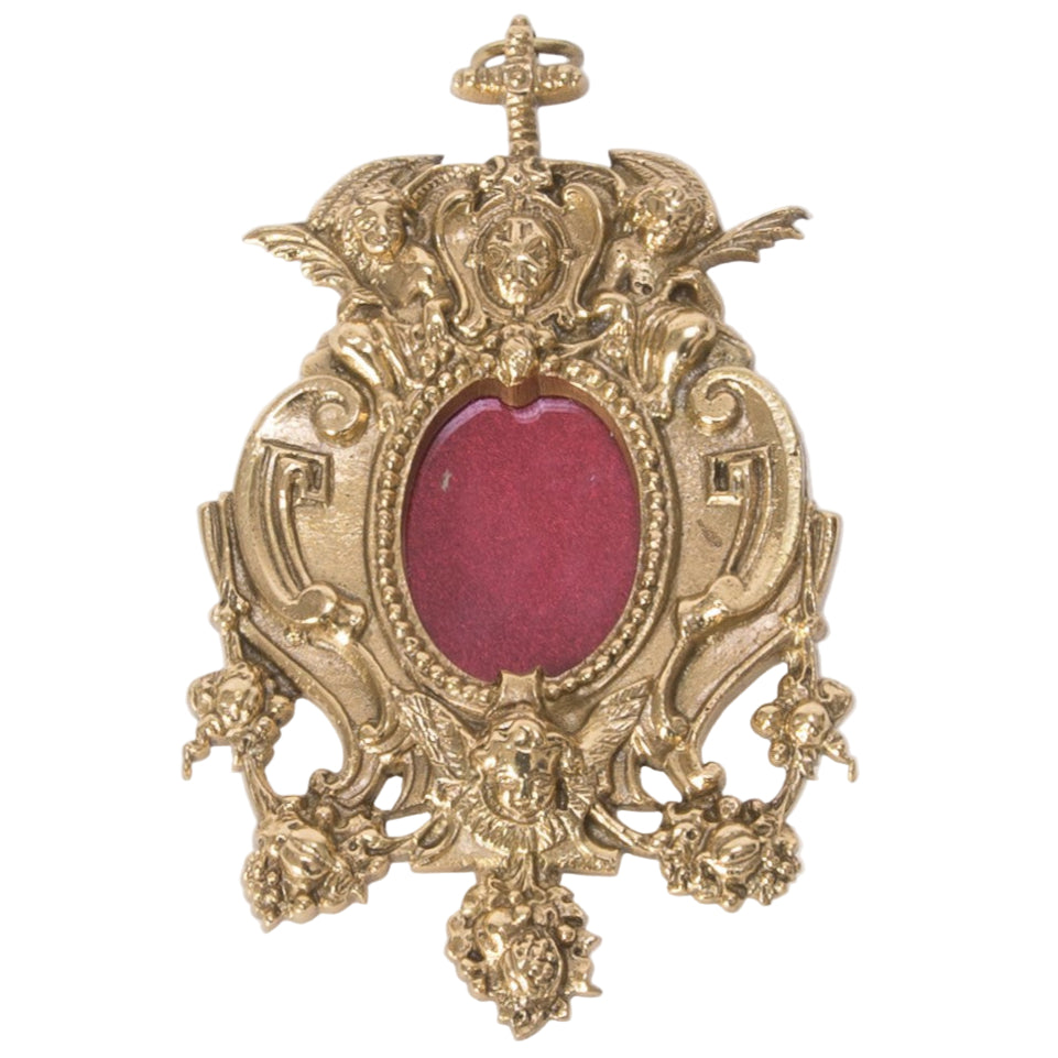 A polished brass and lacquered gold hanging reliquary with a front glass view and a relic compartment, featuring intricate architectural details. Has a hook on the top for wall hanging.