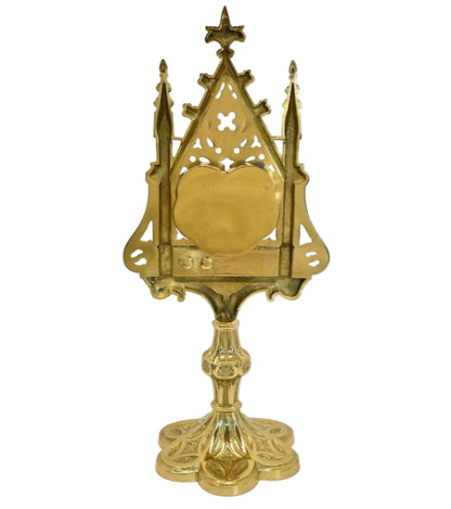 A polished brass and lacquered Gothic reliquary with a relic compartment and a heart-shaped glass opening in the center. Removable back door to house your relic.